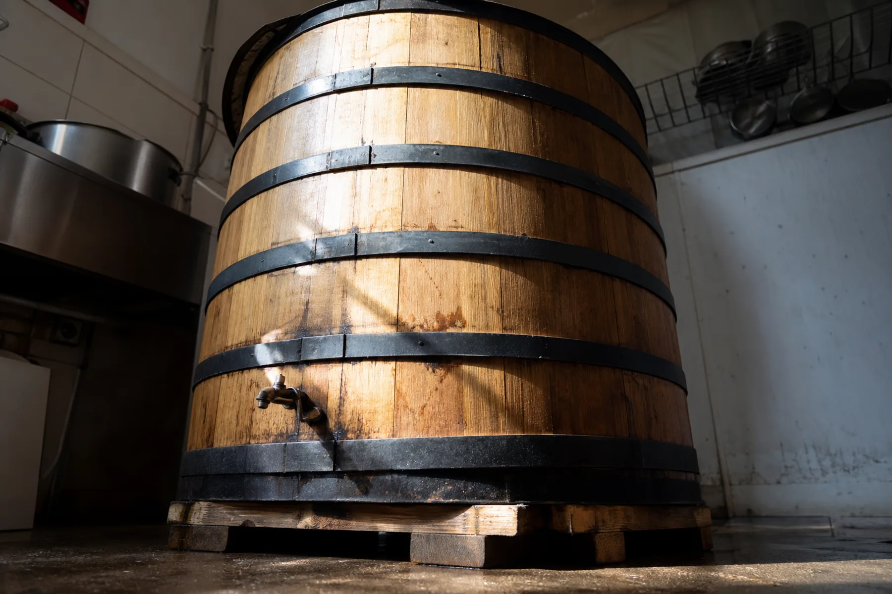 A row of large oak vats bound with iron hoops standing against a cellar wall.