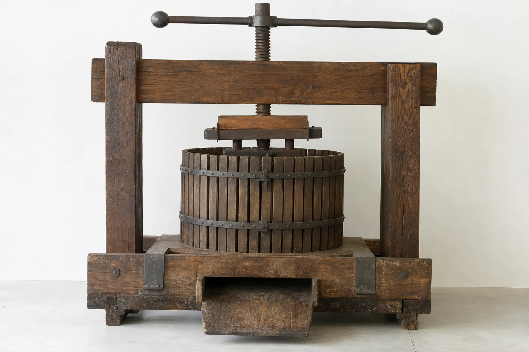 A circular stone trough with an upright stone wheel standing beside a heavy wooden screw press.